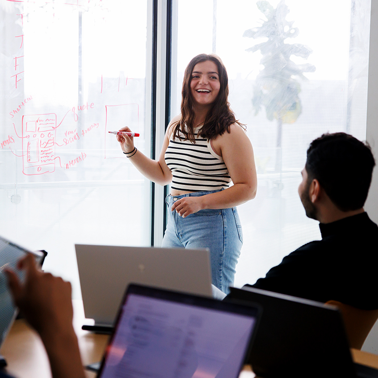A student writes on a window with a dry-erase marker while working on a group project.